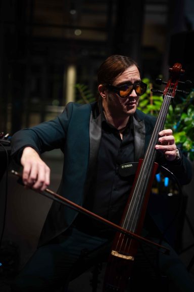 Entertainment bei Business Events Mann in eleganter Kleidung spielt Cello in einem modernen, beleuchteten Raum.