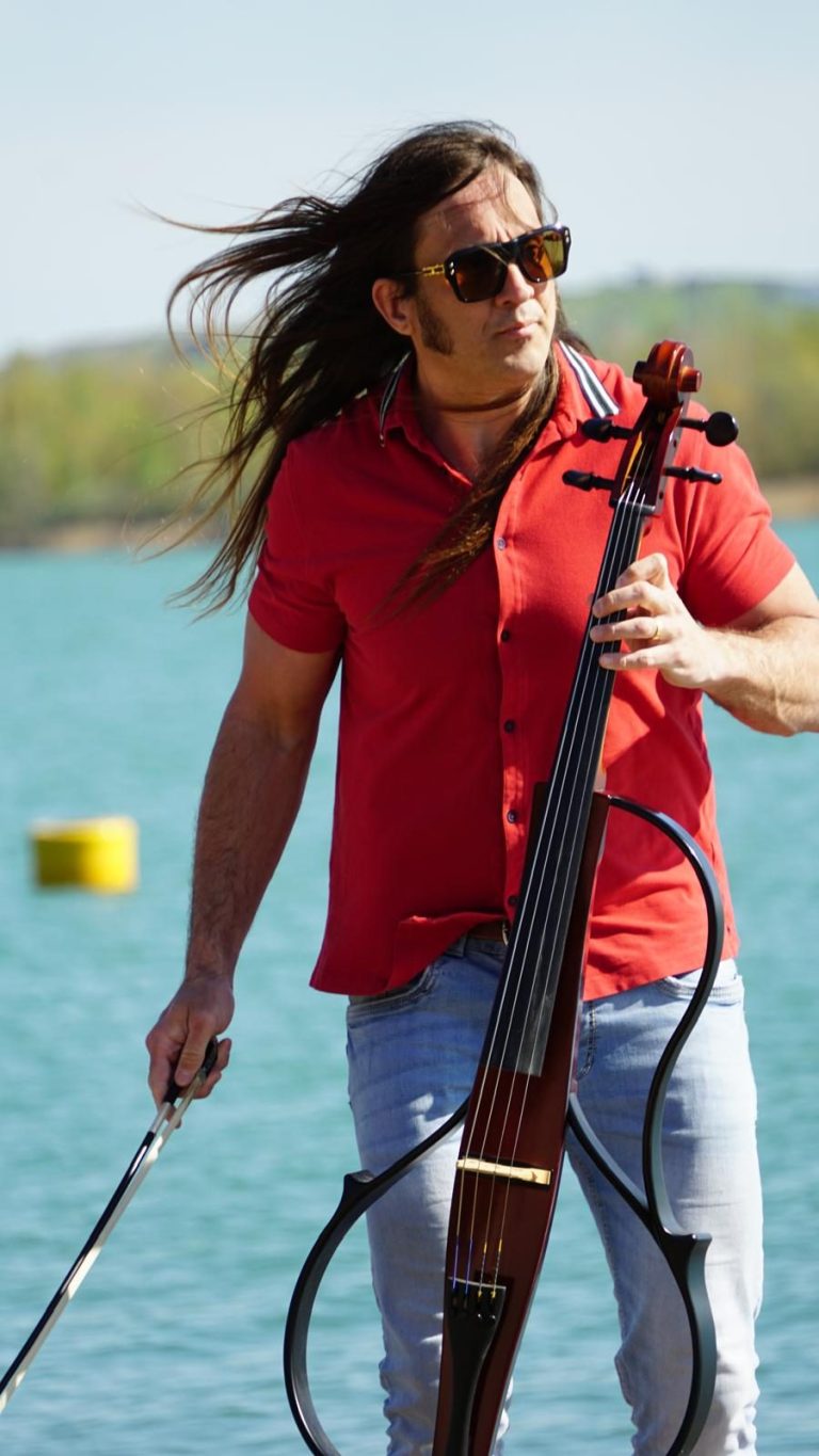 eleganter Live Musiker für besondere Anlässe Mann in weißem Anzug spielt ein Cello in einer parkähnlichen Umgebung.